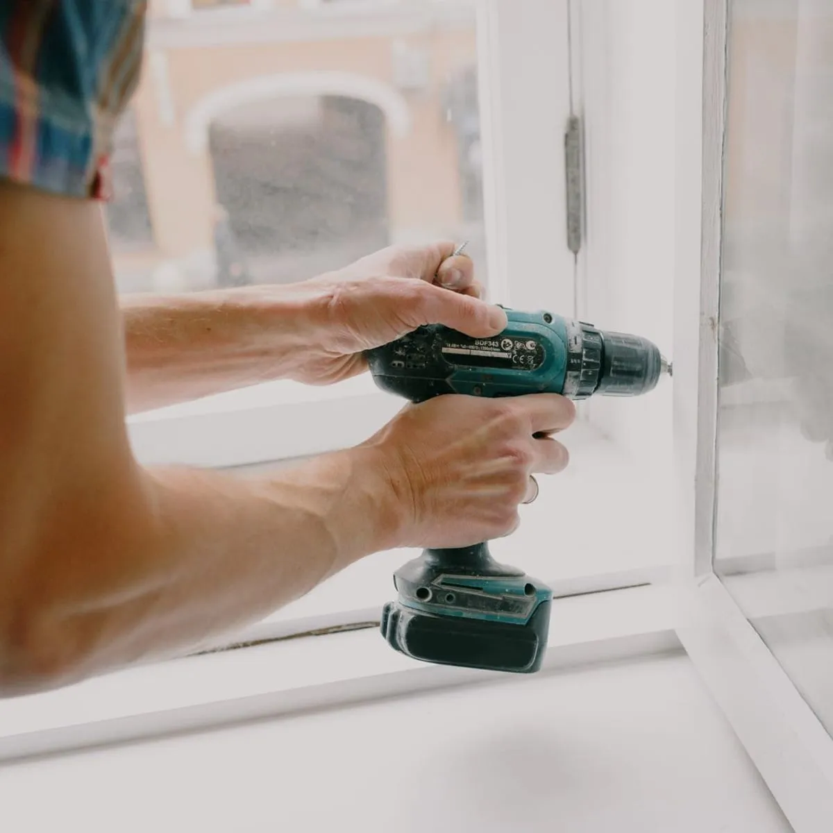 Installer fastening a replacement window frame with a cordless drill